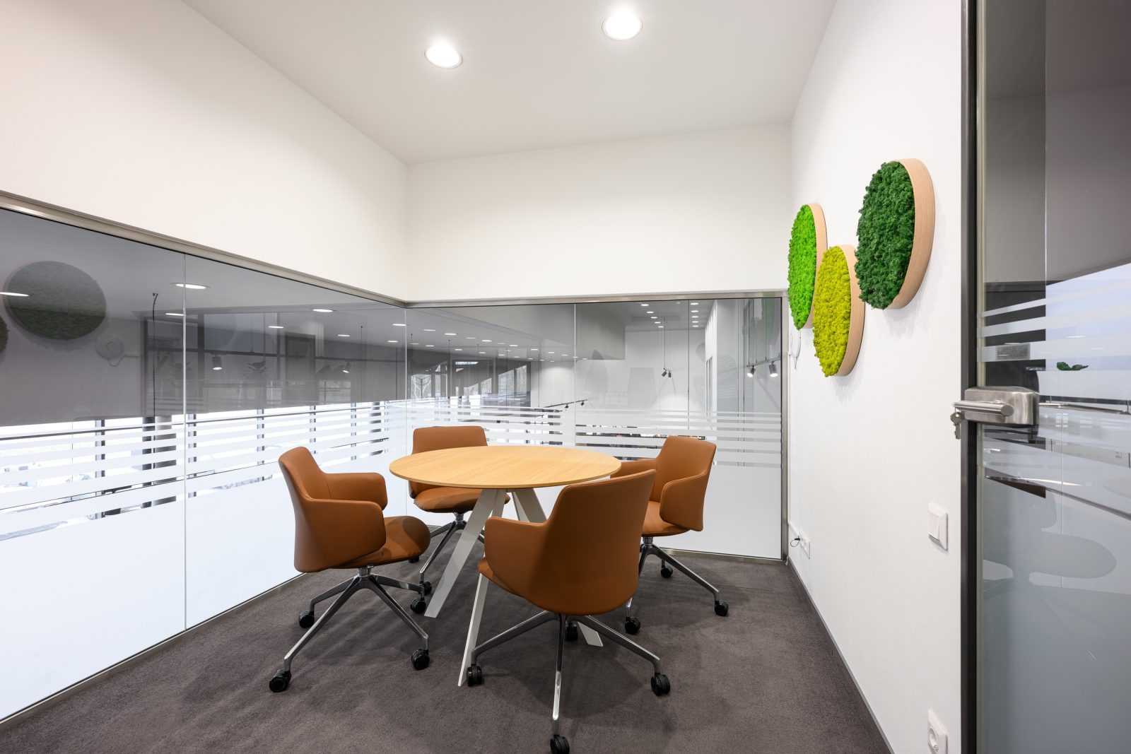 Modern office meeting room with round table, orange chairs, and green wall decor.