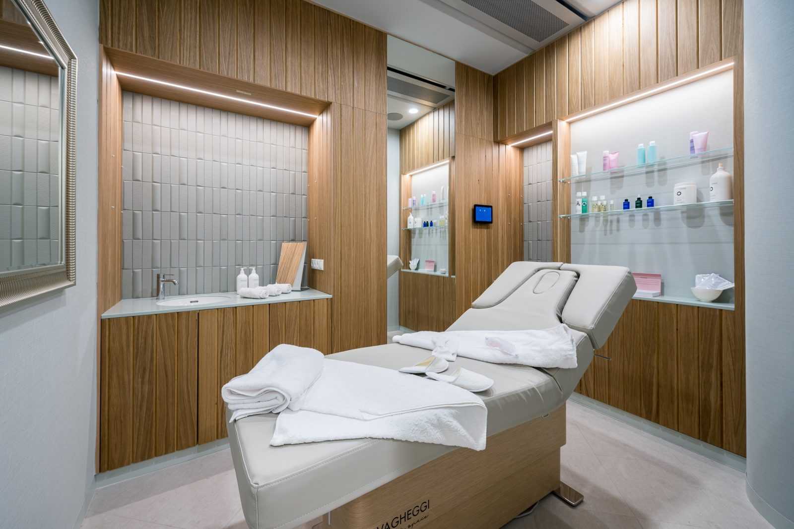 Modern spa treatment room with wooden walls and white massage bed.