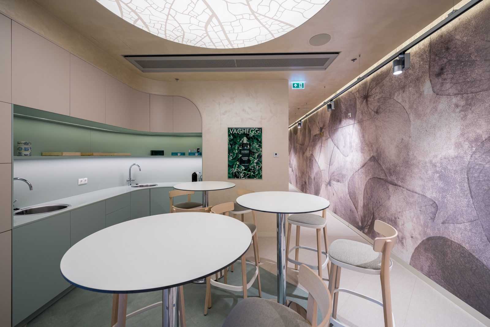 Modern interior with round tables, leaf-patterned wall, and curved kitchenette.