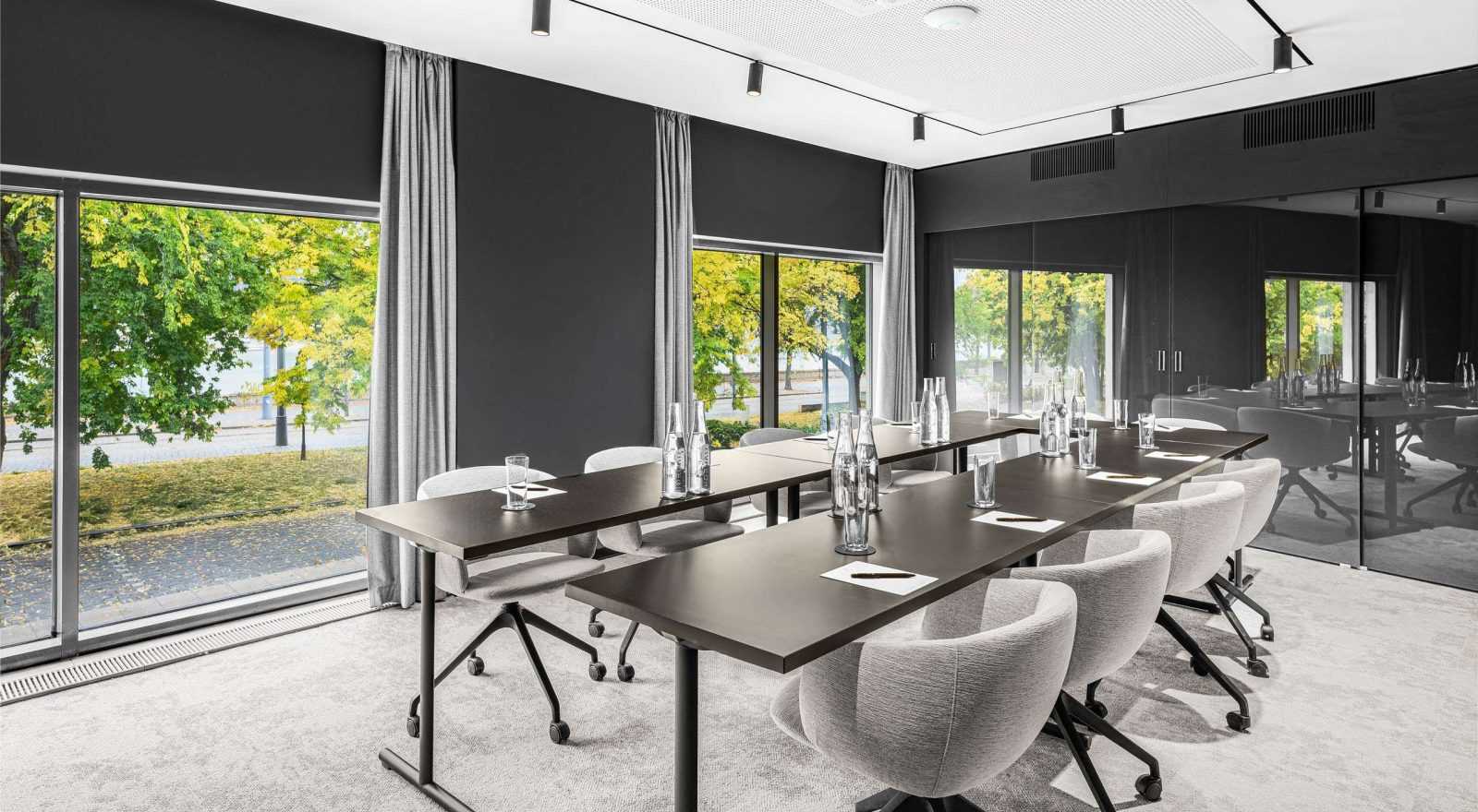 Modern conference room with long table and chairs, large windows overlooking greenery.