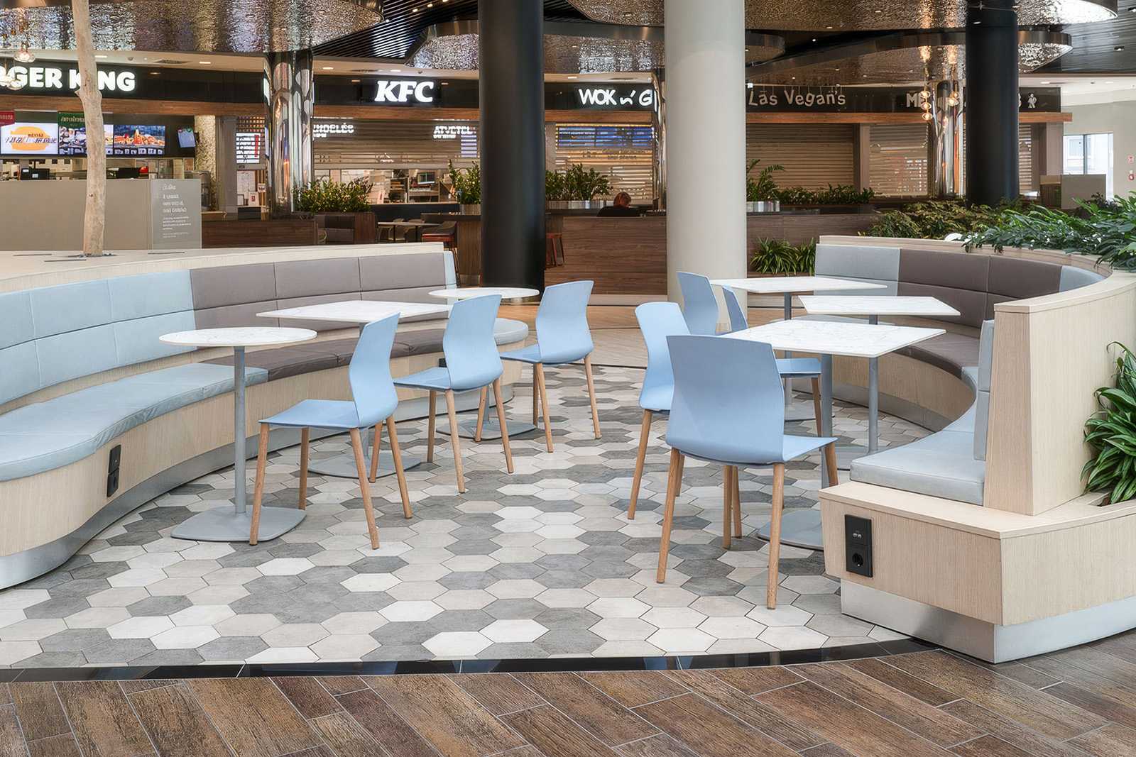 Modern curved seating area with light blue chairs and hexagonal tile flooring in a food court.