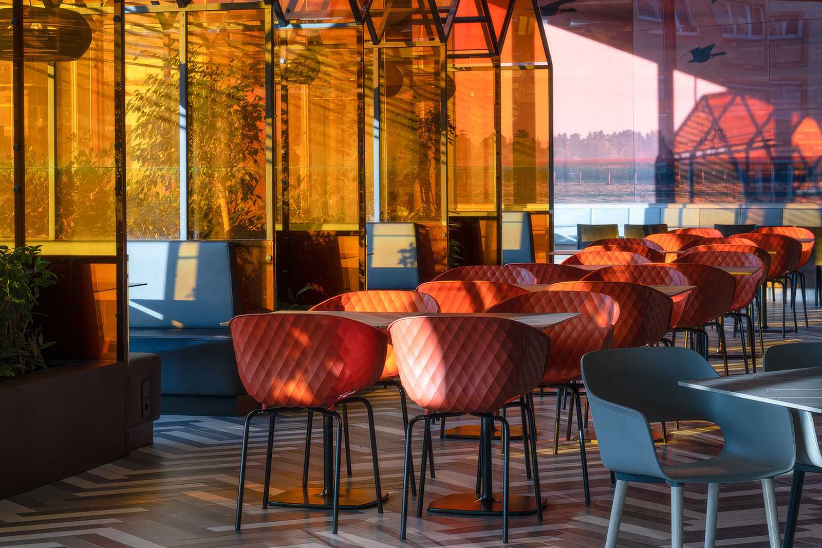 Modern restaurant interior with orange chairs and glass walls.