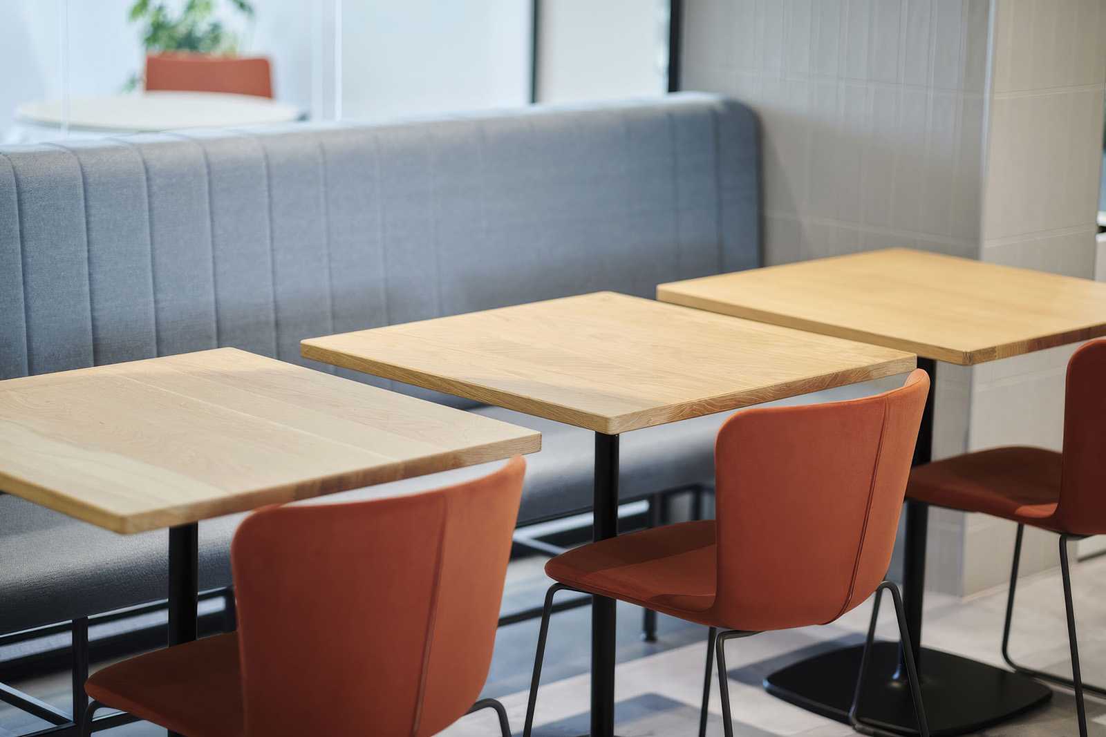 Modern wooden tables and orange chairs in a stylish cafe setting.
