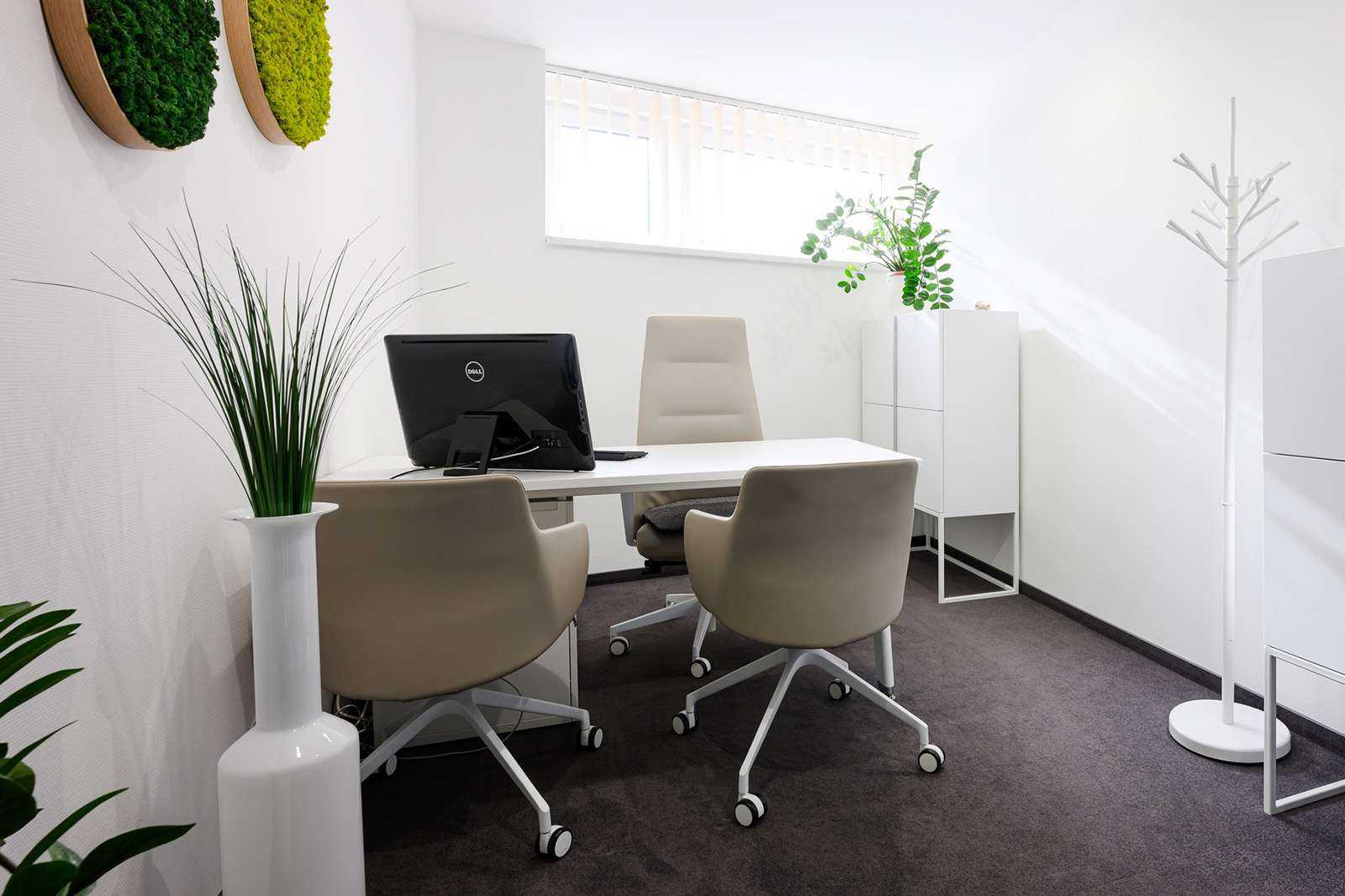 Modern office space with white desk, beige chairs, and green plants for a clean workspace.