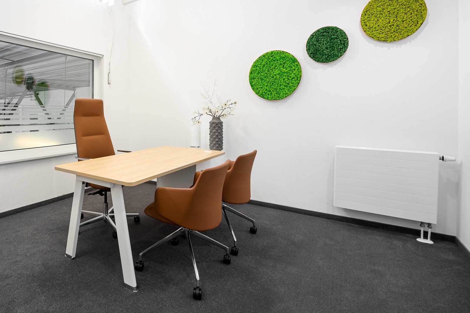Modern office meeting room with wooden table, brown chairs, and green moss wall art.