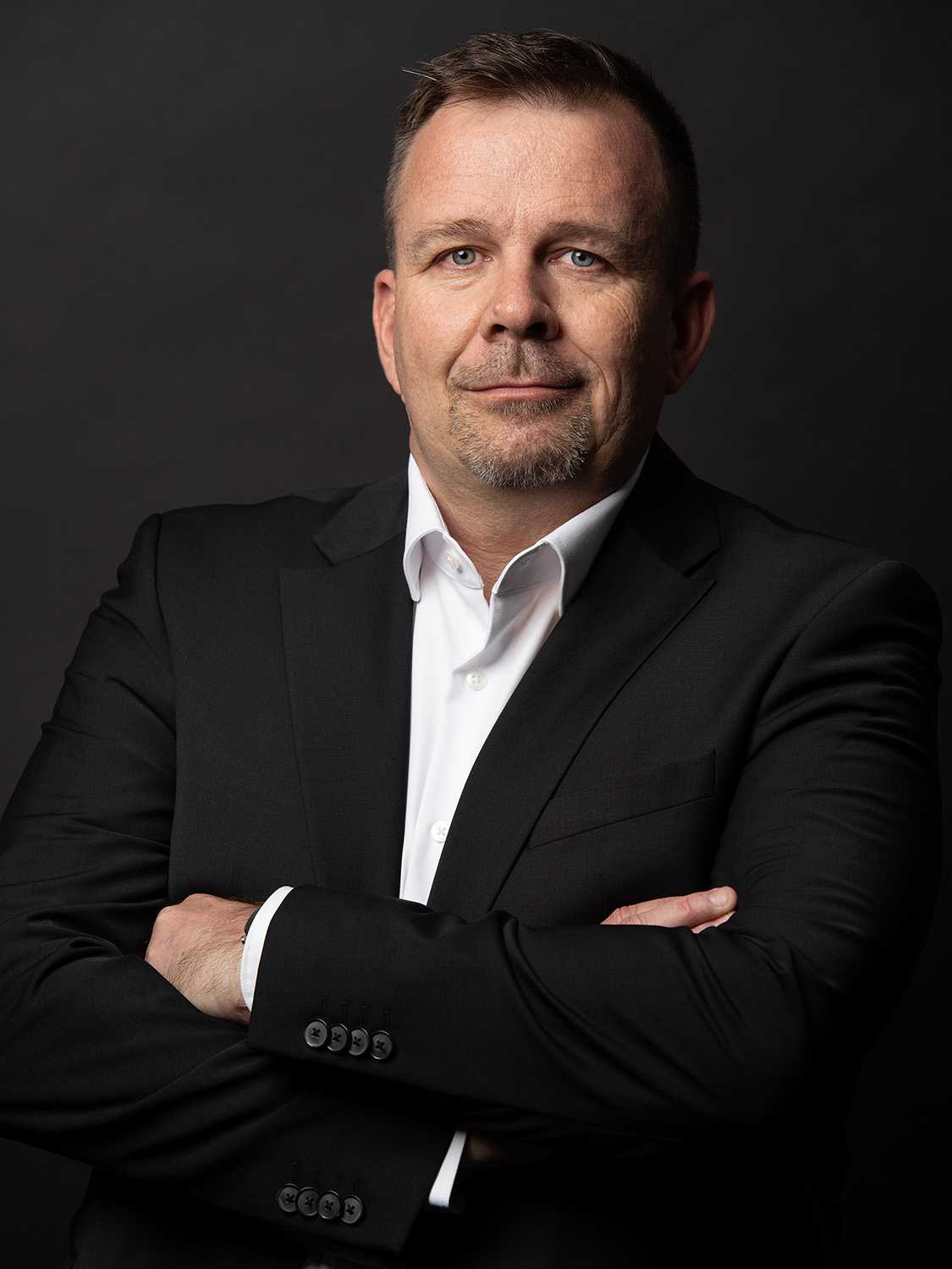 Professional portrait of a man in black suit and white shirt with arms crossed.