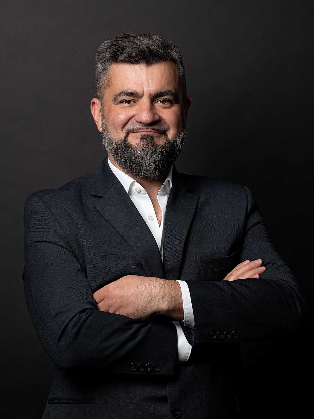 Professional portrait of a bearded man in suit with arms crossed.