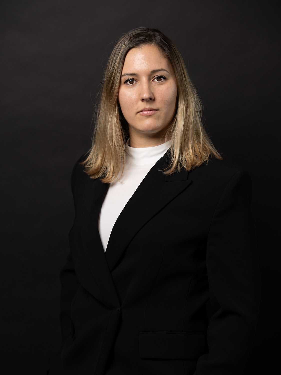 Professional woman in black blazer and white turtleneck against dark background.
