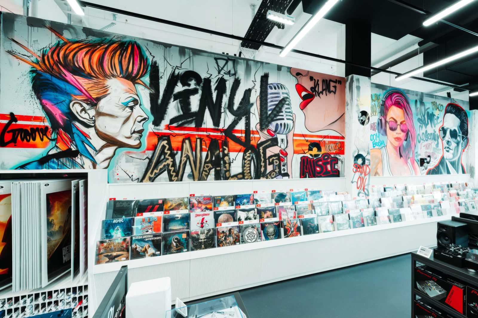 Vibrant graffiti wall with 'Vinyl Analog' text above rows of vinyl records in a music store.