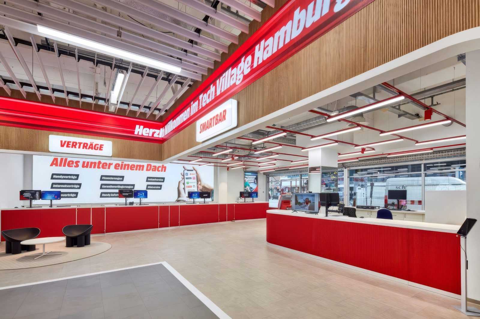 Modern Tech Village Hamburg store interior with red counters and digital displays.
