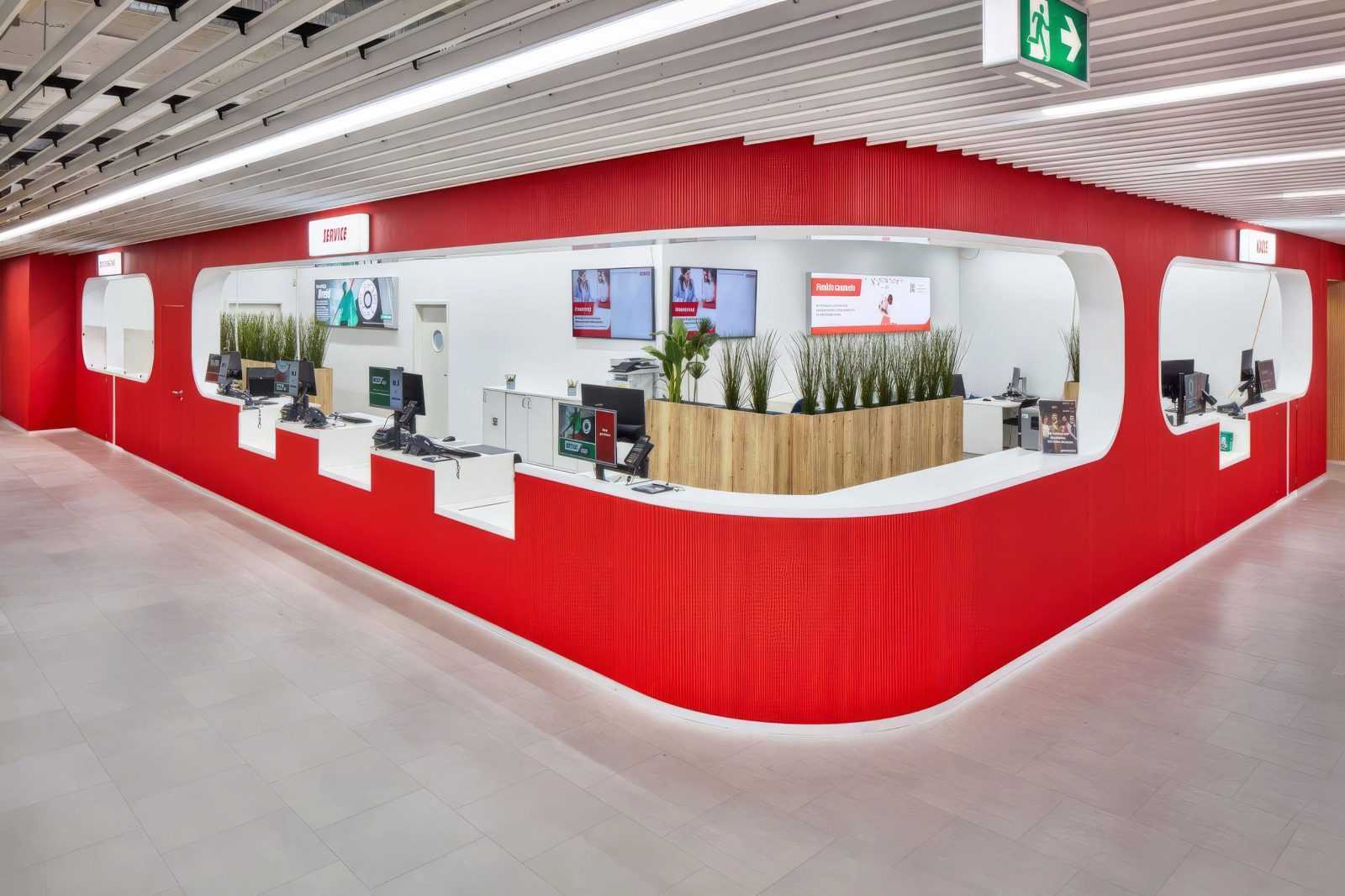 Modern red and white customer service desk at Megaholz with computers and greenery.