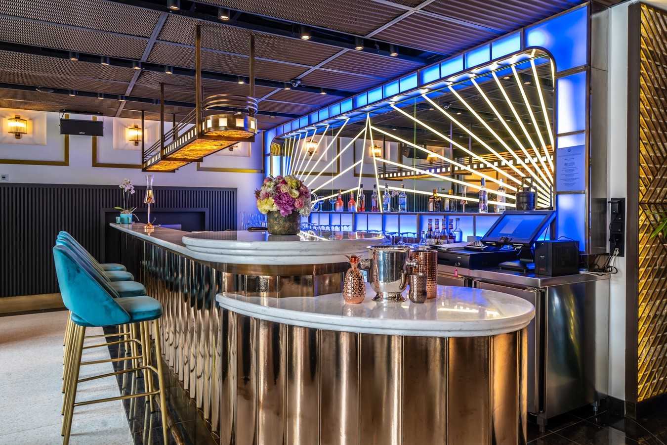 Modern luxury bar with gold accents and blue lighting.