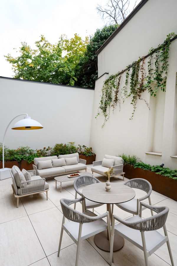 Modern outdoor patio with white furniture and greenery.