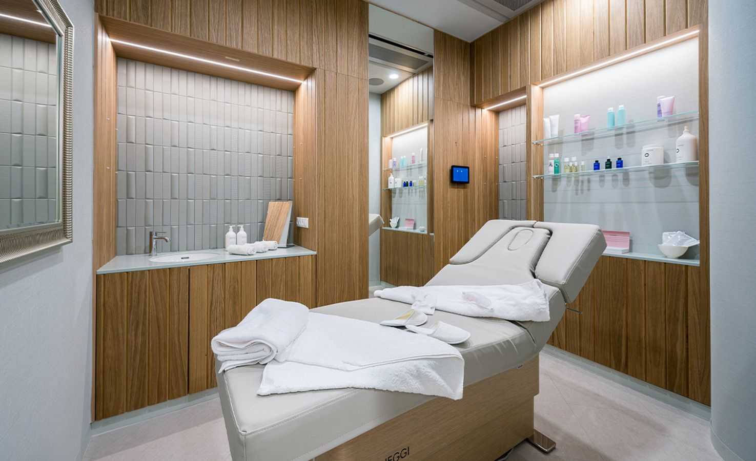 Modern spa treatment room with wooden walls and white massage table.