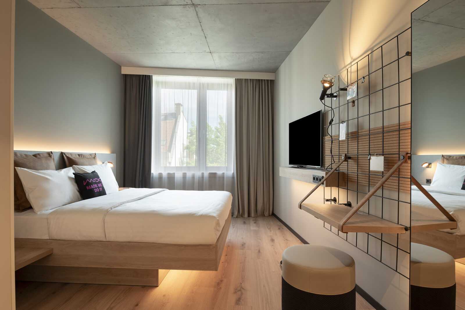Modern hotel room with wooden bed, large window, and industrial design.