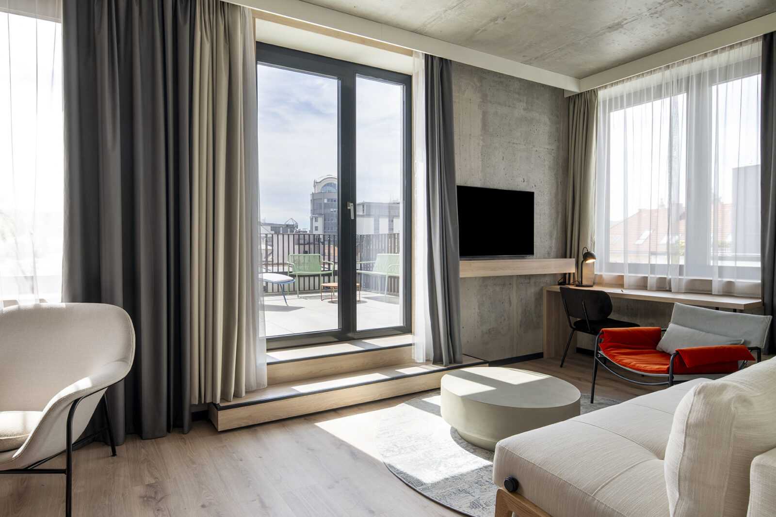 Modern hotel room with large windows and balcony view.