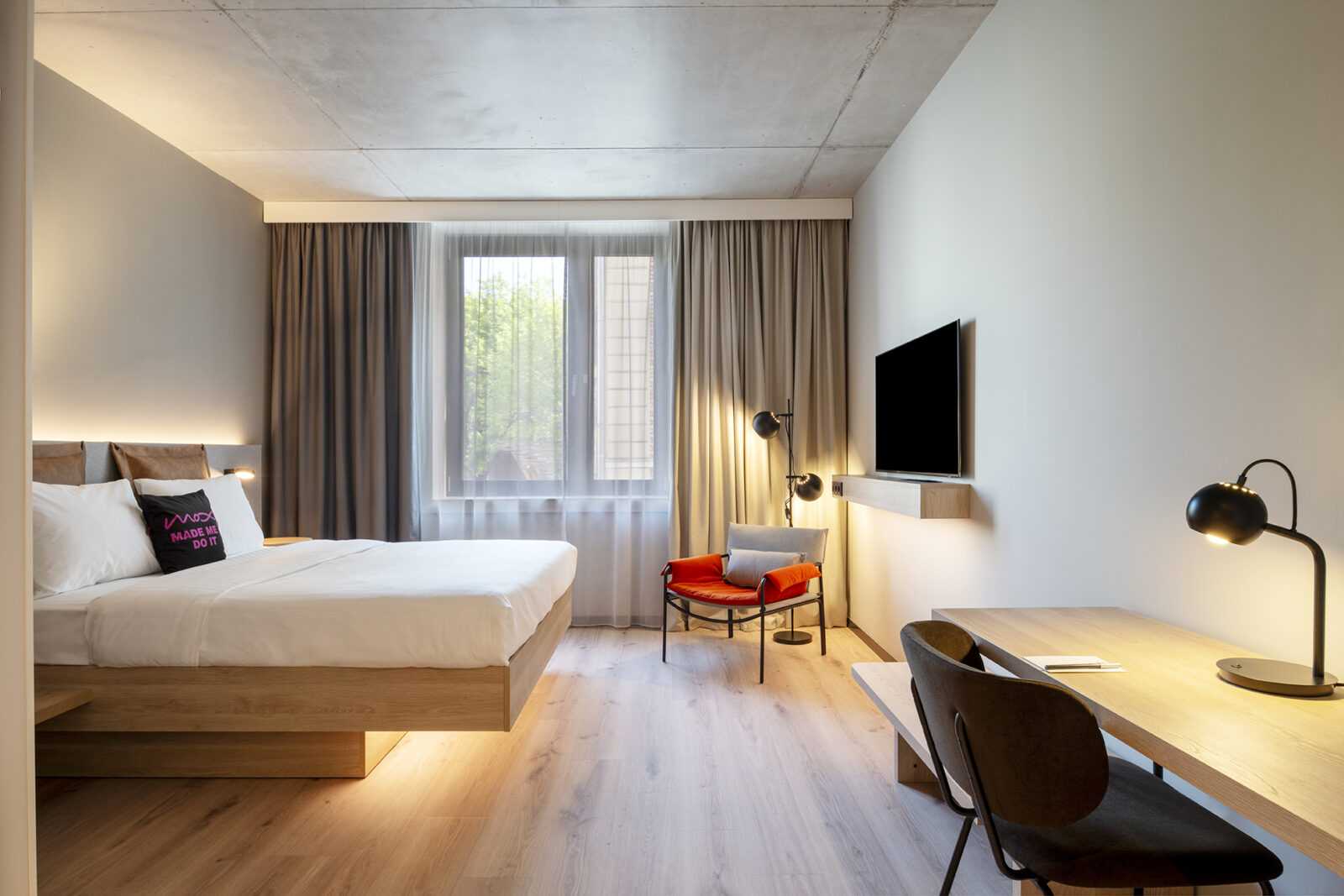 Modern hotel room with wooden bed, desk, and red chair at Megaholz.