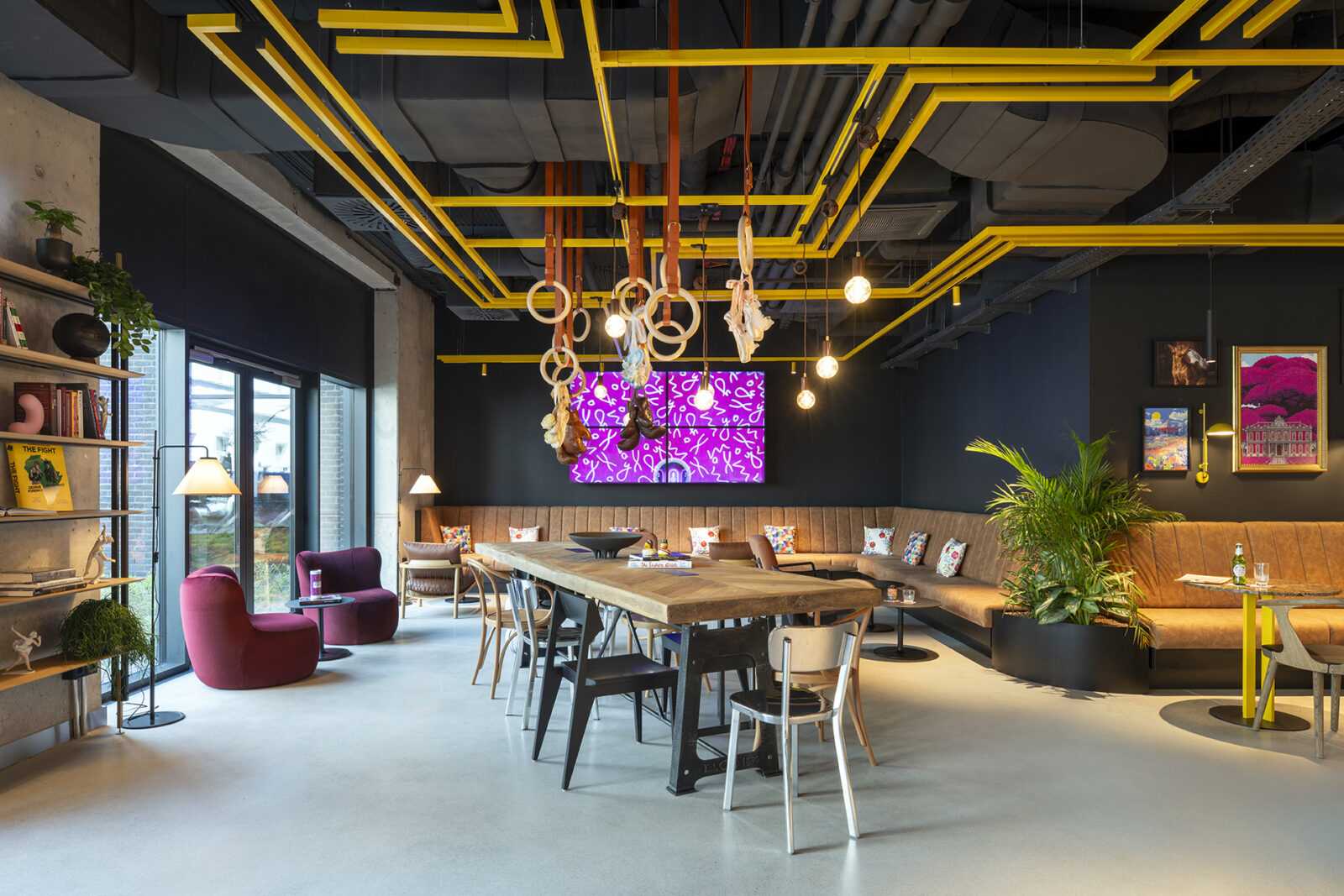Modern industrial lounge with yellow ceiling beams and colorful furniture.