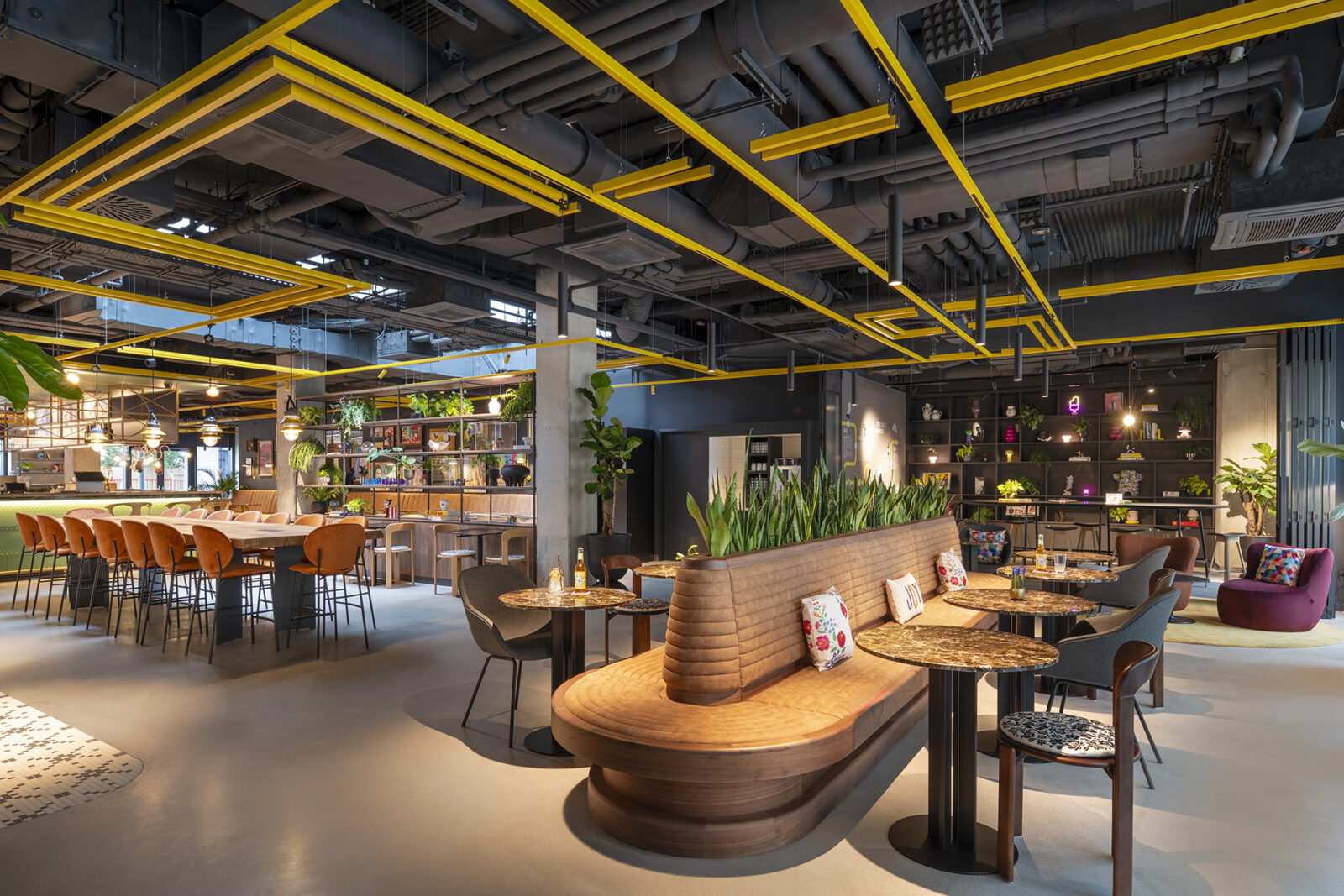 Modern industrial cafe interior with yellow ceiling beams and wooden seating.
